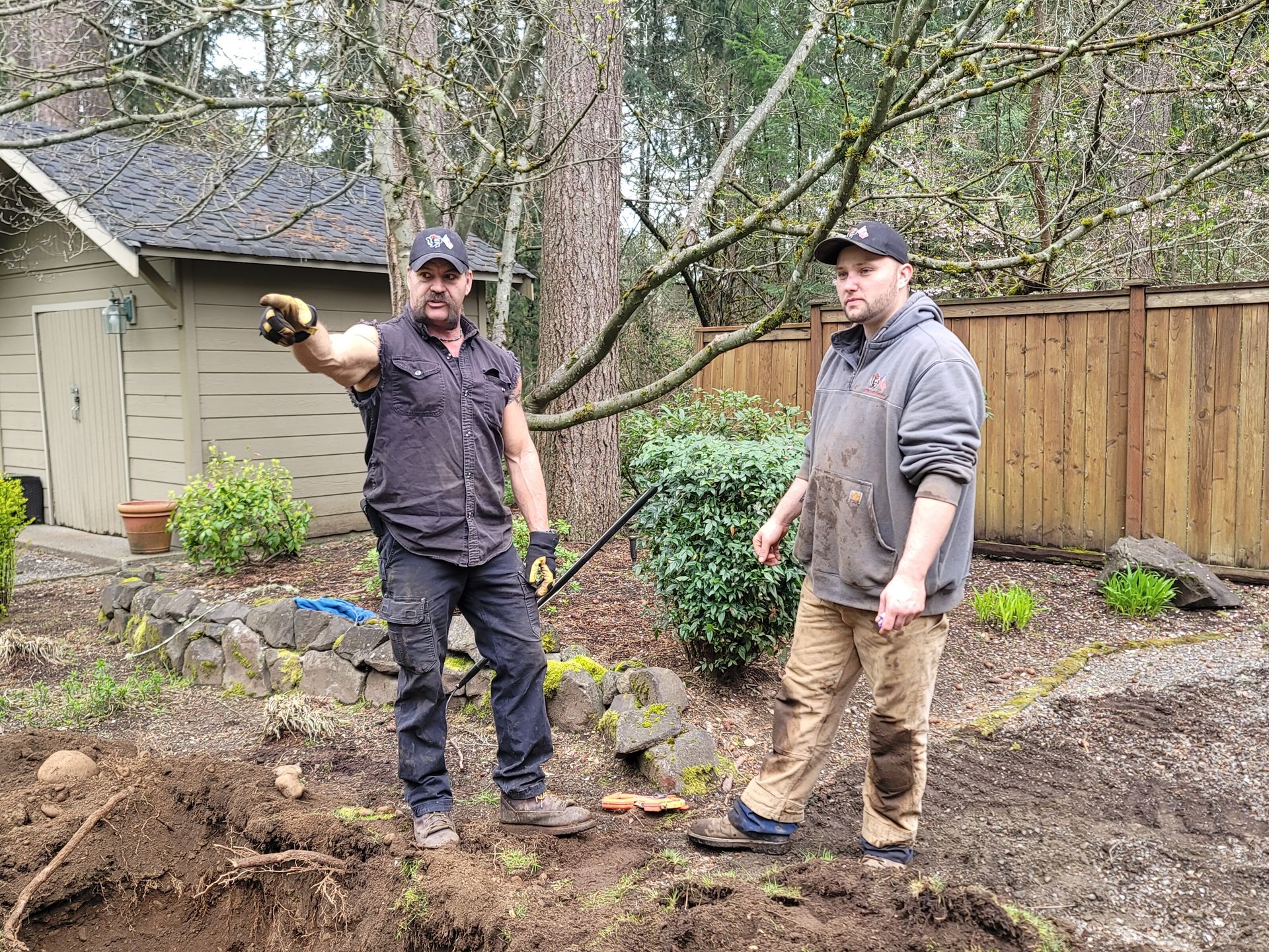 Two men are standing in the dirt in front of a house.