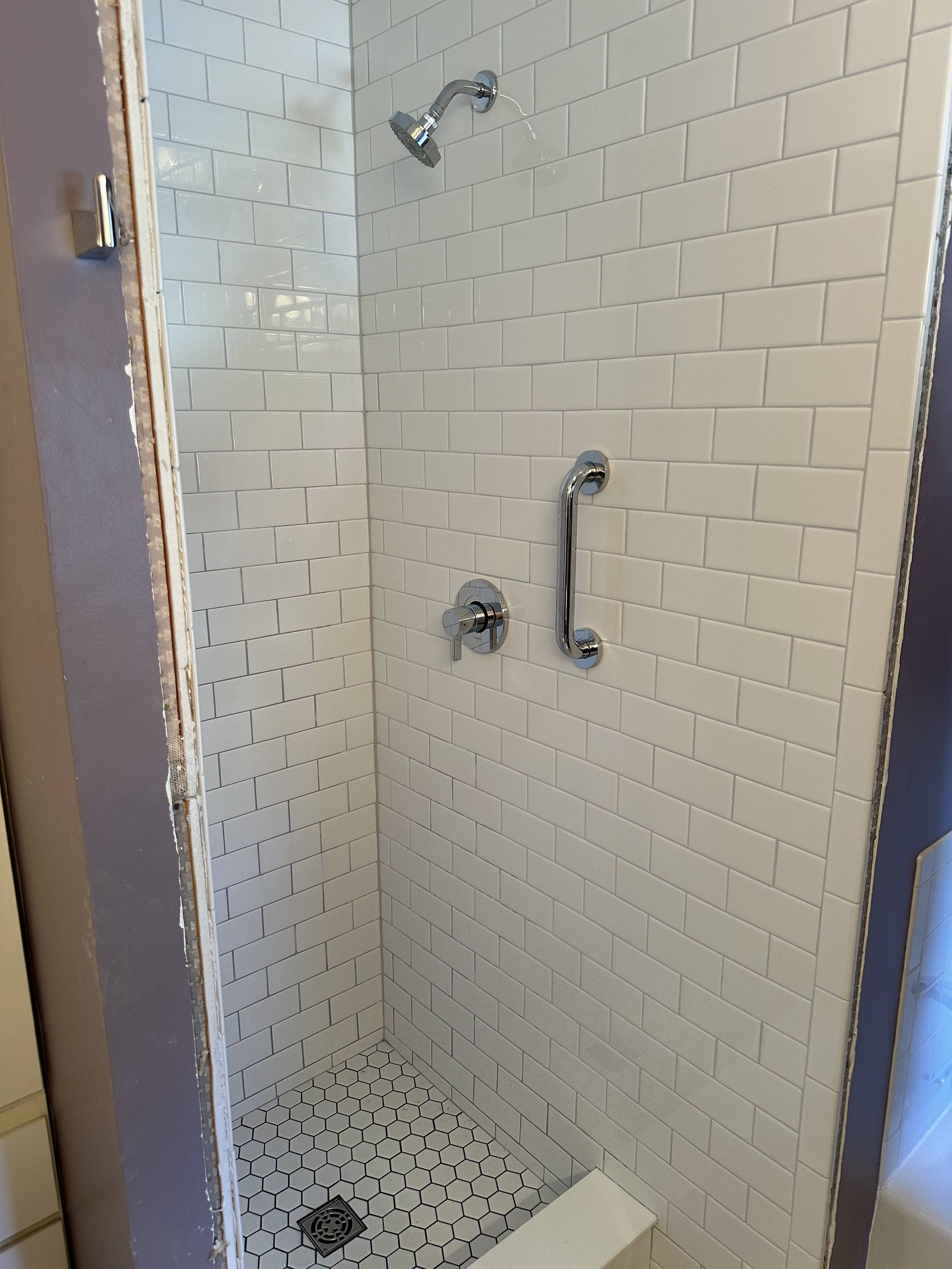 A shower with white tiles and a hand rail