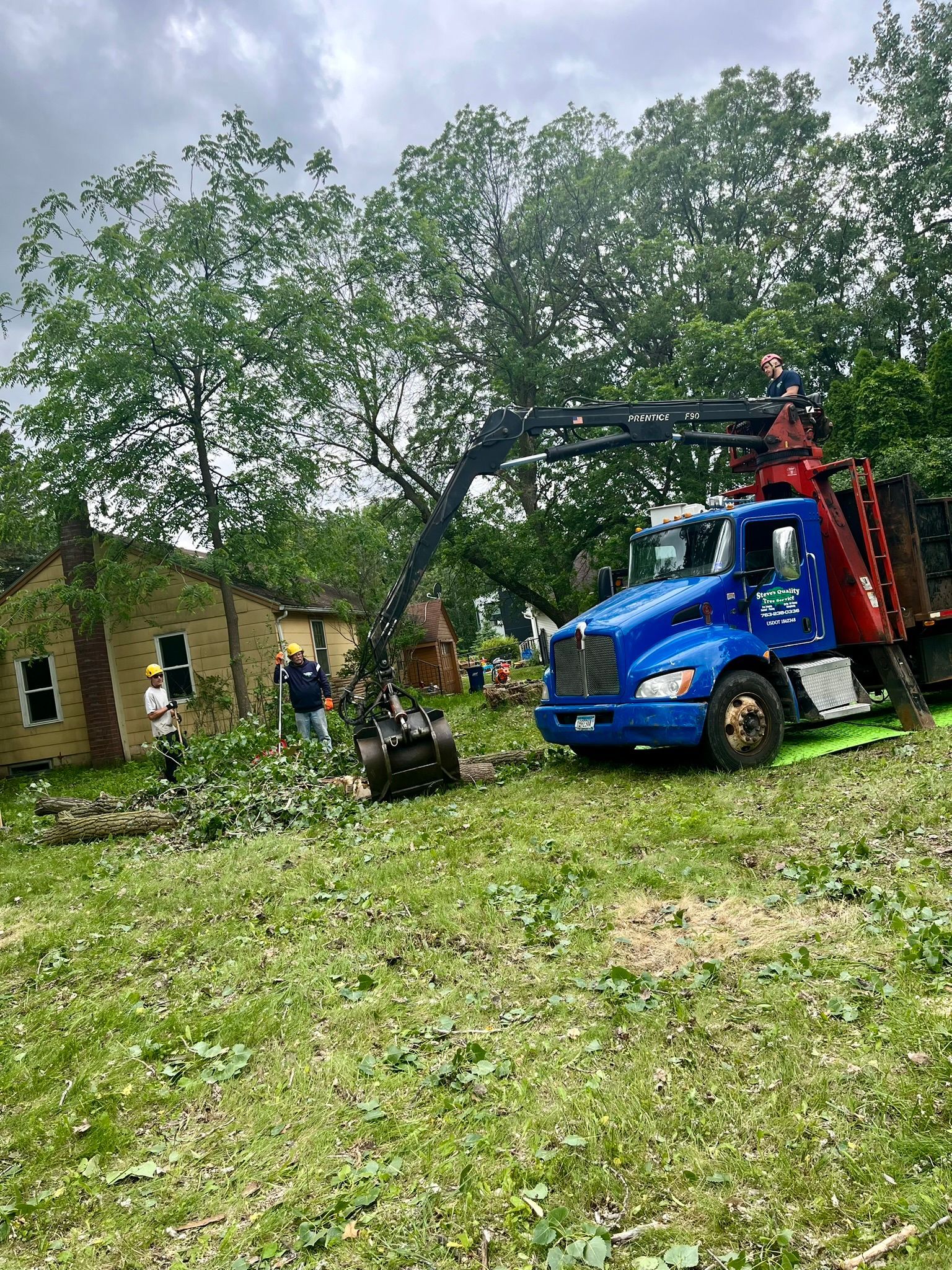A blue truck with a crane attached to it is parked in a grassy field.
