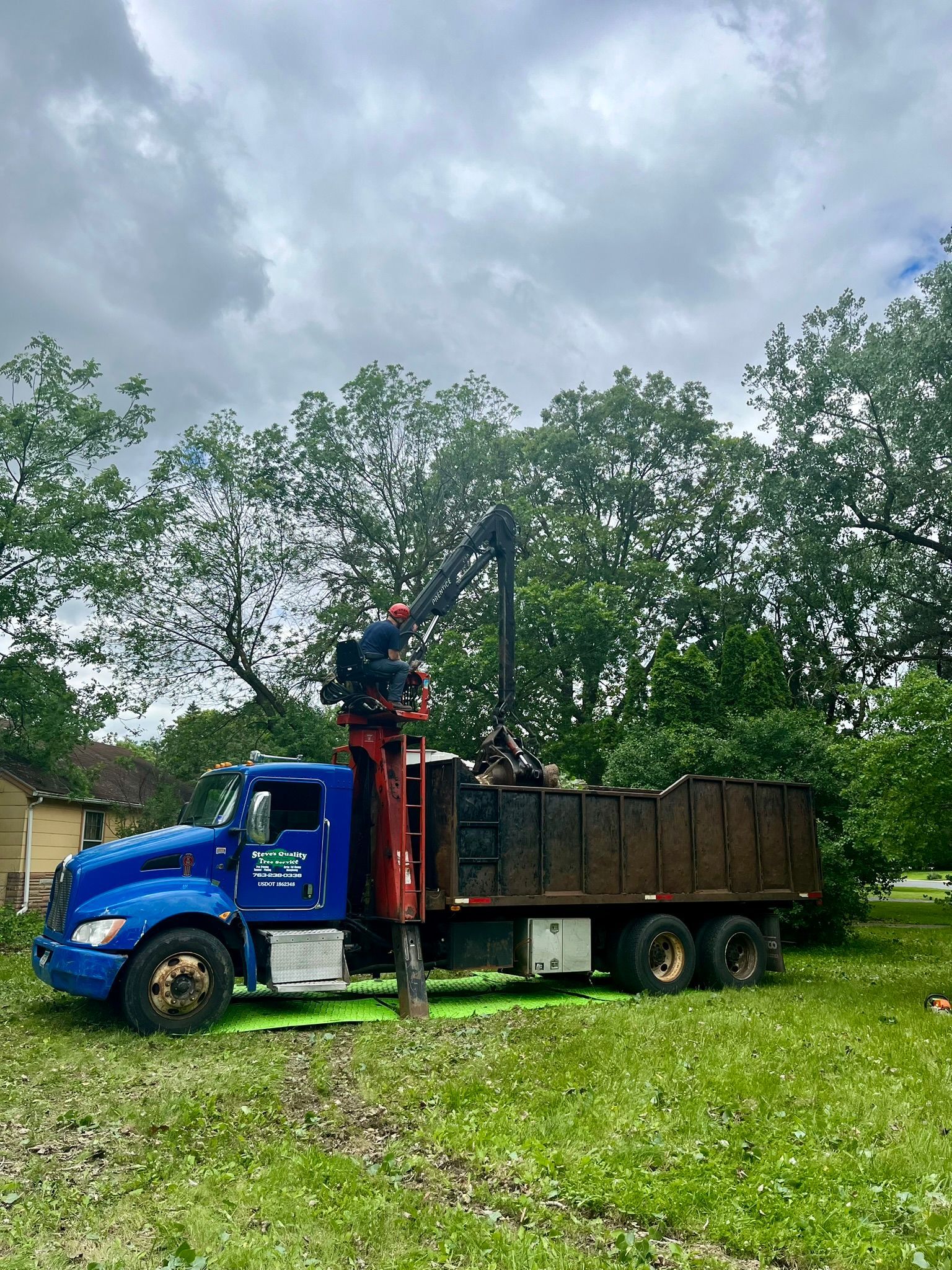 A blue dump truck with a crane attached to it is parked in a grassy field.