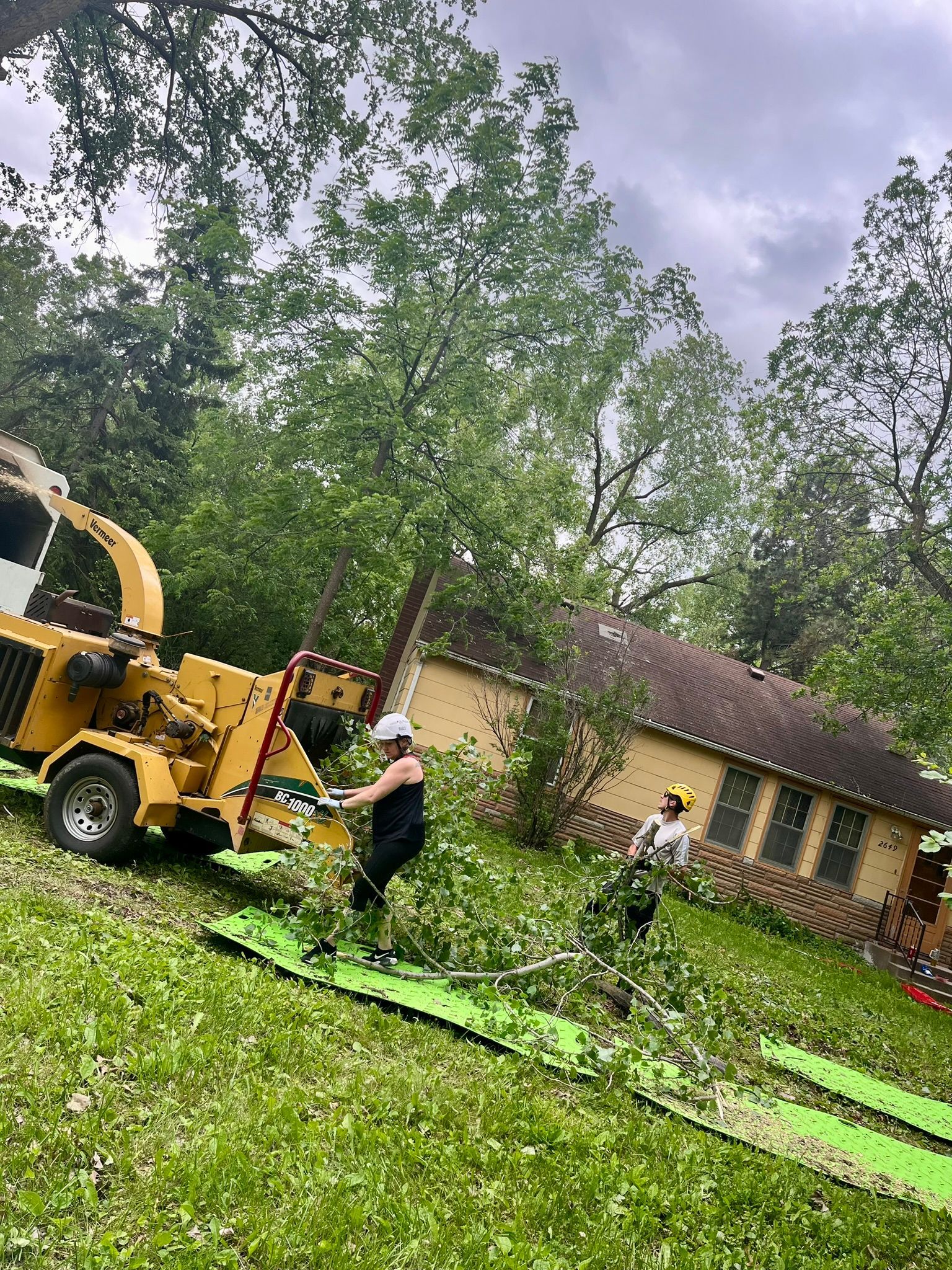 A woman is standing next to a tree chipper in a yard.