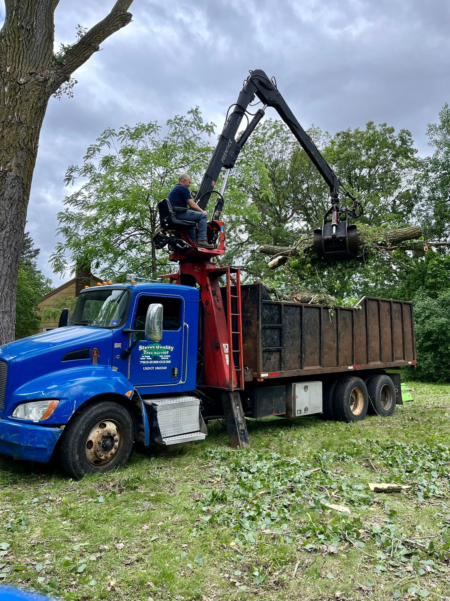 A man is sitting on top of a blue truck with a crane attached to it.