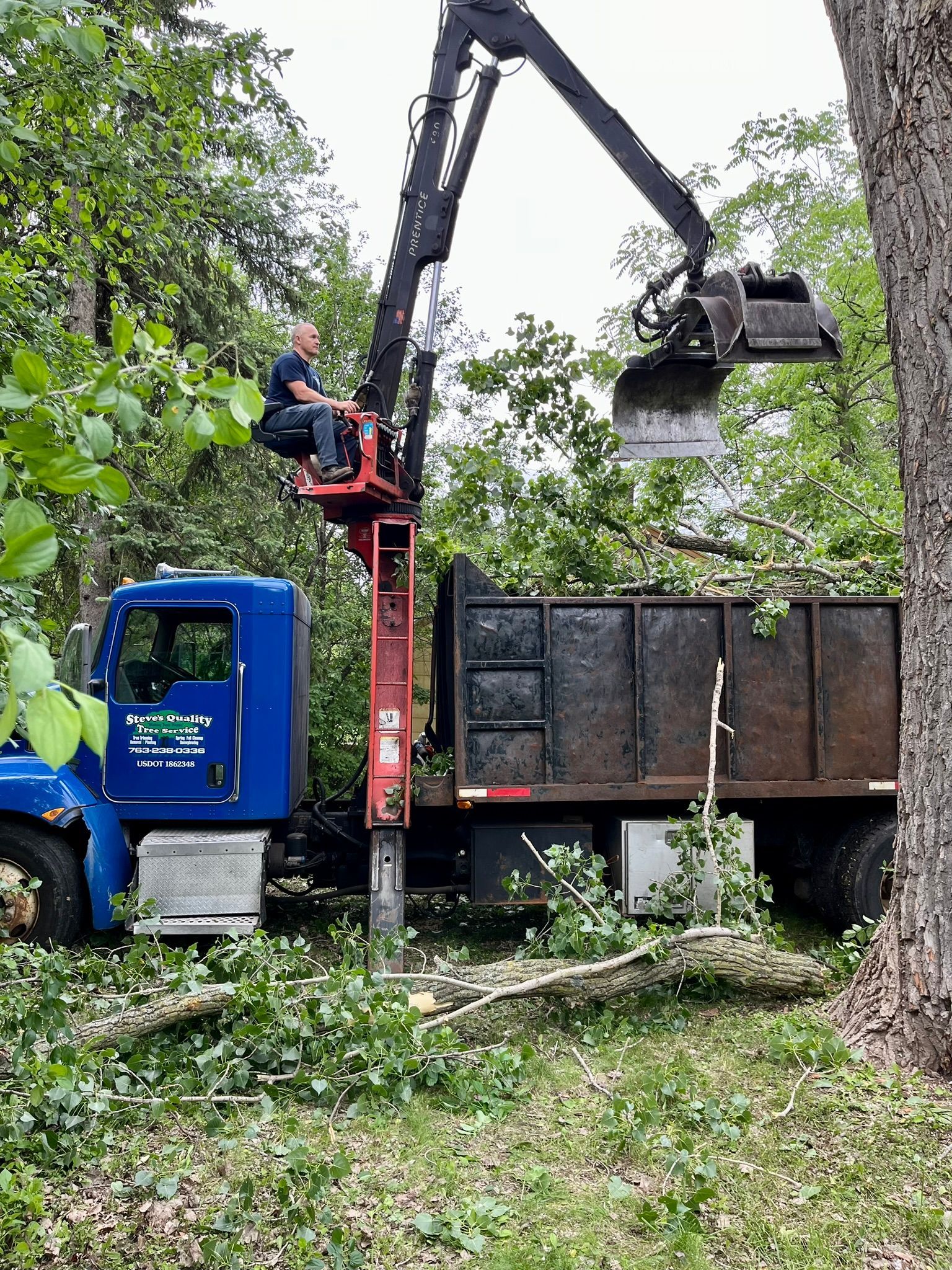 A man is sitting on top of a crane next to a dump truck.