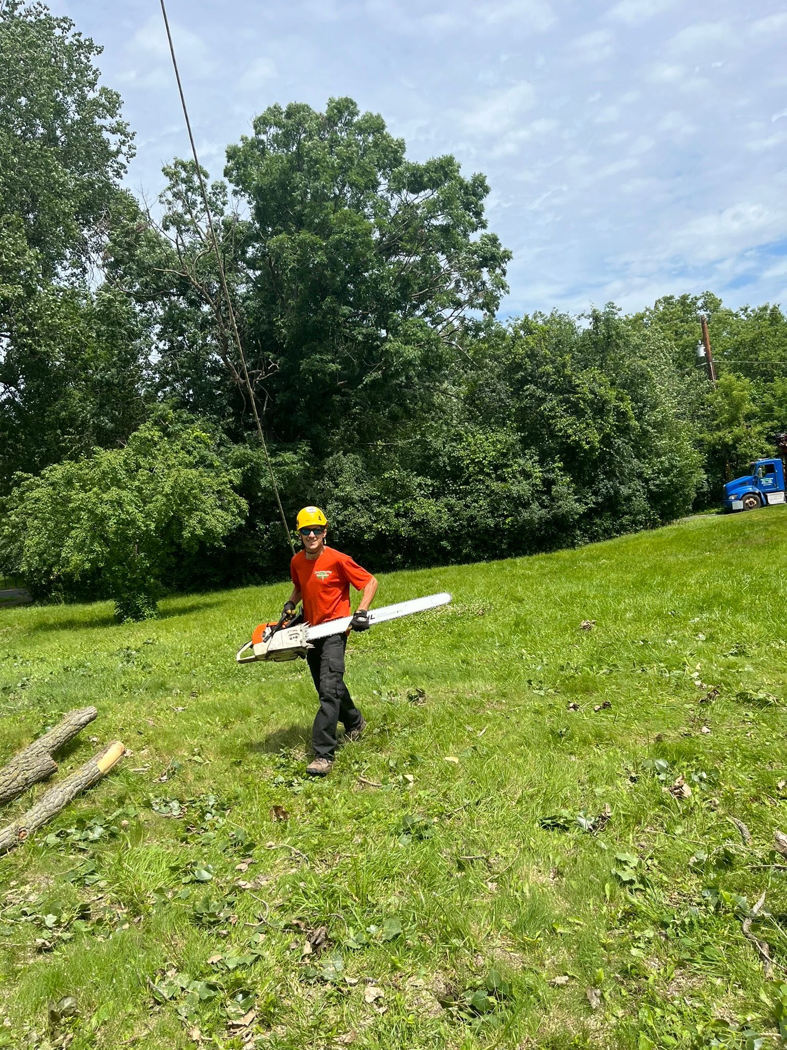 A man is standing in a grassy field holding a chainsaw.