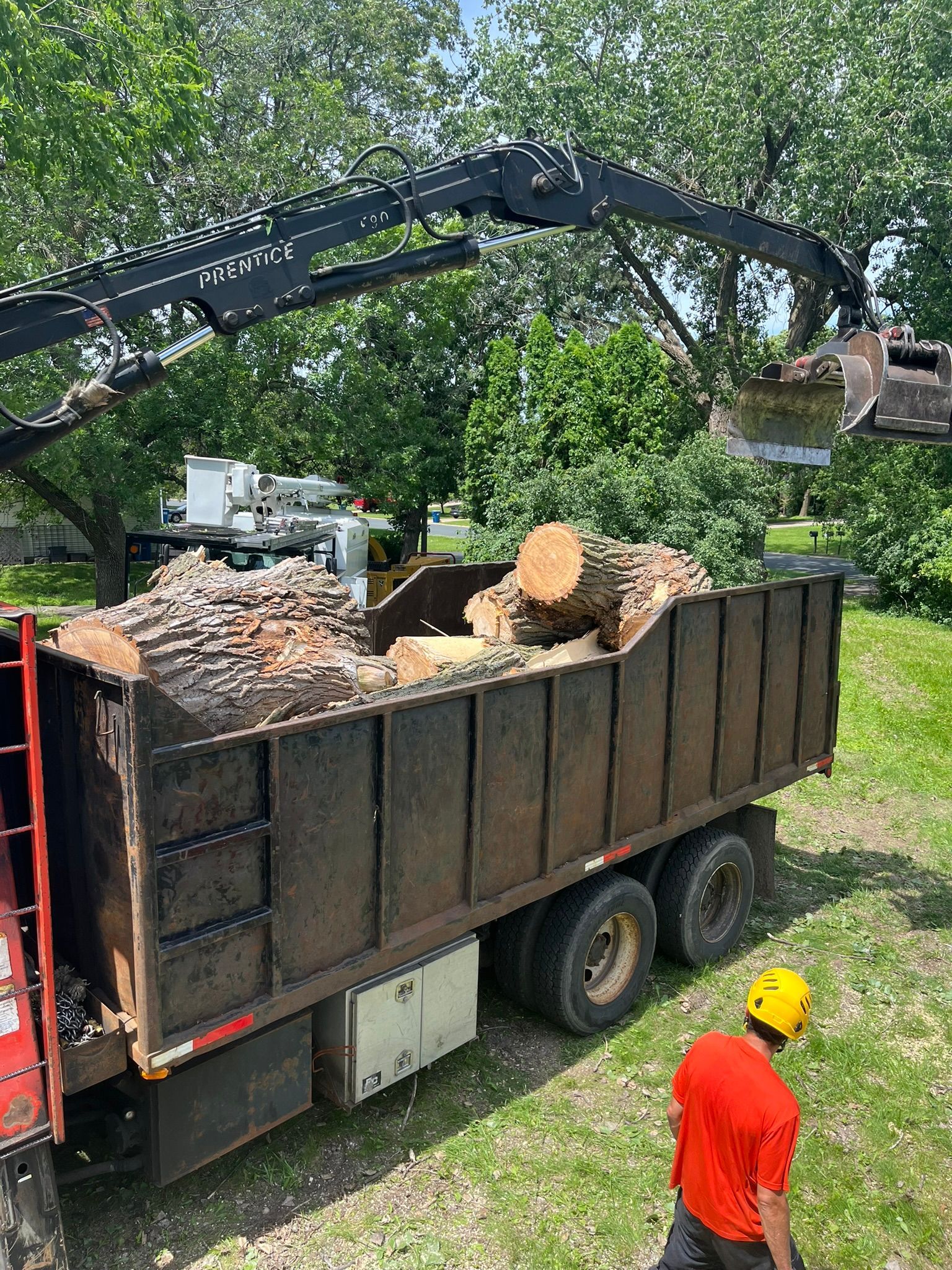 A man is standing next to a dump truck filled with logs.