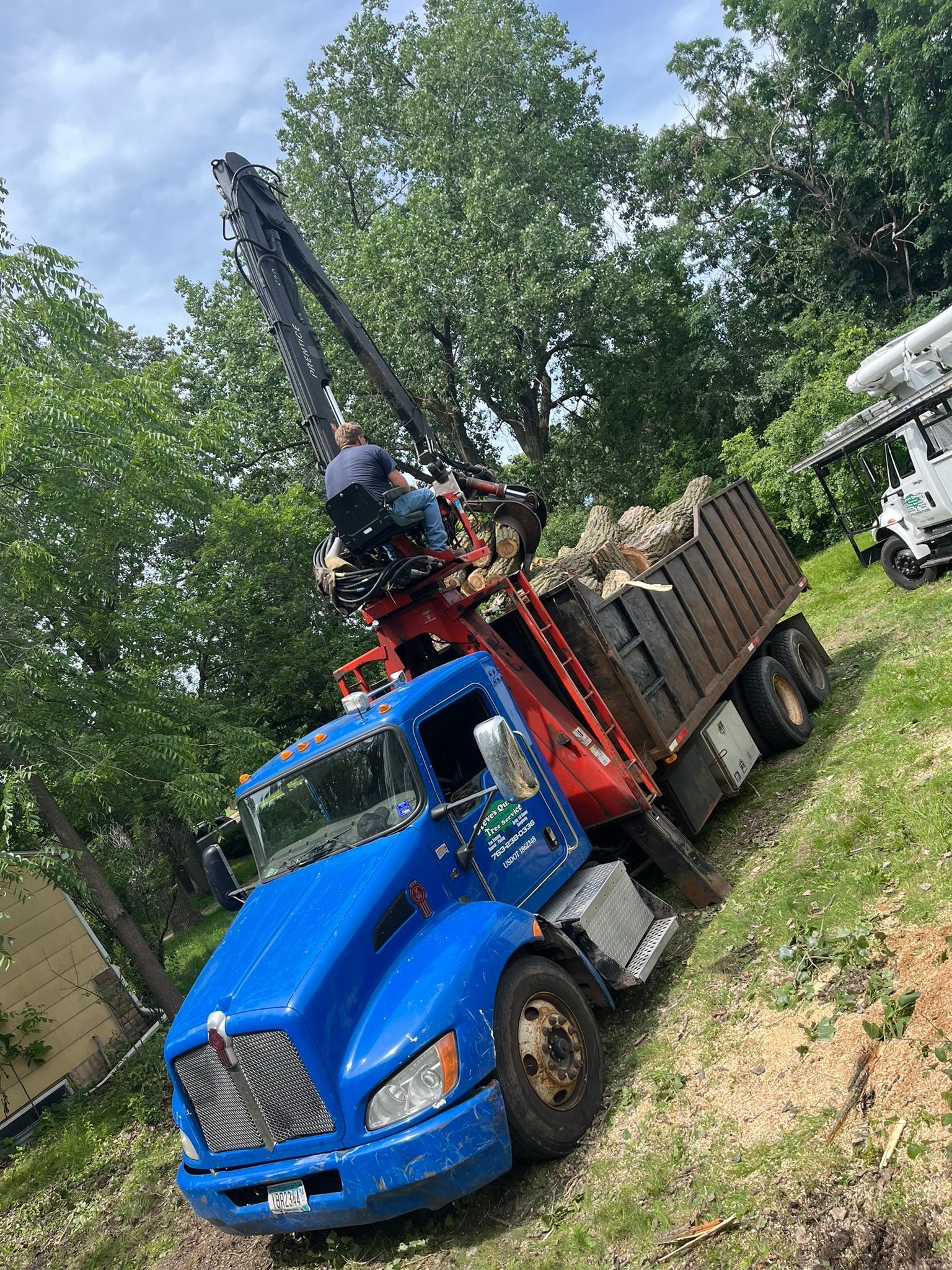 A blue truck with a crane attached to it is parked in a grassy field.