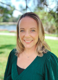 Woman with blonde hair smiles, wearing a green dress, in a park.