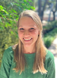 Blonde woman smiling in a green sweater, trees in the background.
