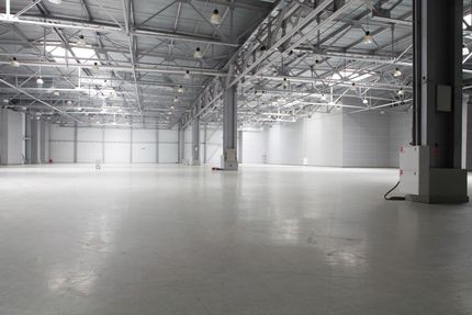 Empty industrial warehouse with a polished concrete floor and metal truss ceiling, lit by bright overhead lights