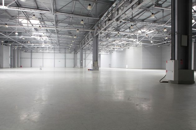 Empty industrial warehouse with a polished concrete floor and metal truss ceiling, lit by bright overhead lights