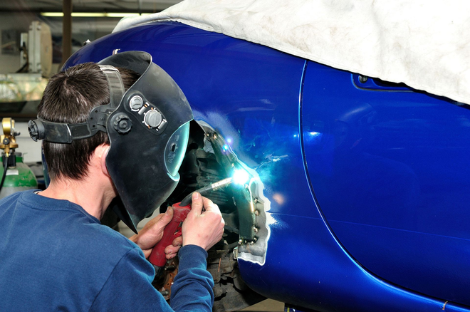 Technician welding a blue aircraft fuselage section in a workshop