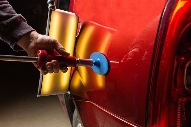 Person polishing a red car with a buffer, creating a shiny finish