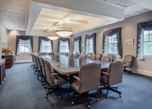 Conference room with long table, striped chairs, and large windows with drapes