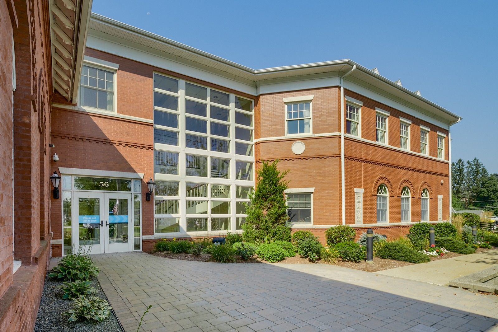 Brick school building entrance with large glass windows and a paved walkway in front
