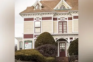 Victorian-style house with beige siding, maroon trim, and trimmed shrubs in front