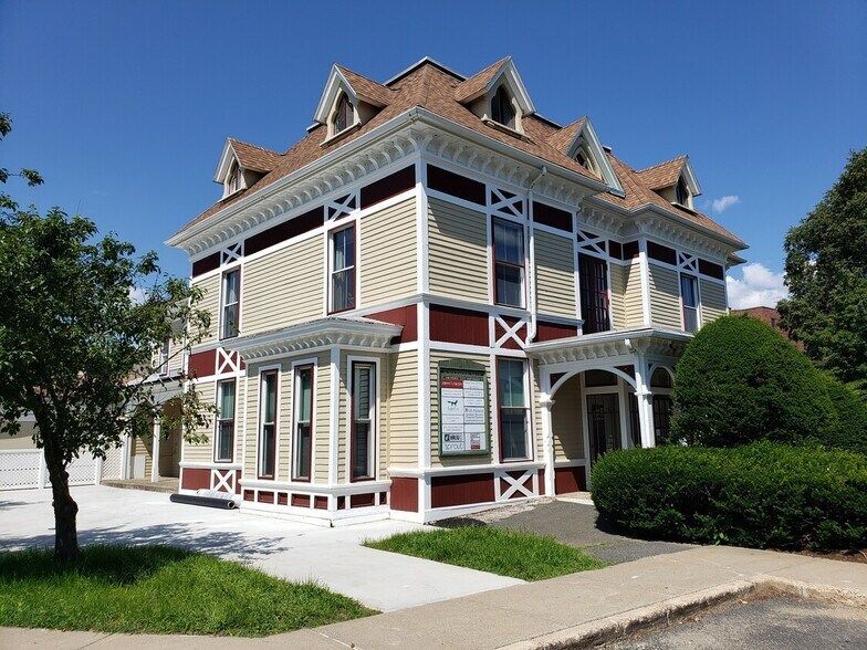 Victorian-style corner house with white trim, red accents, and a steep roof under a blue sky