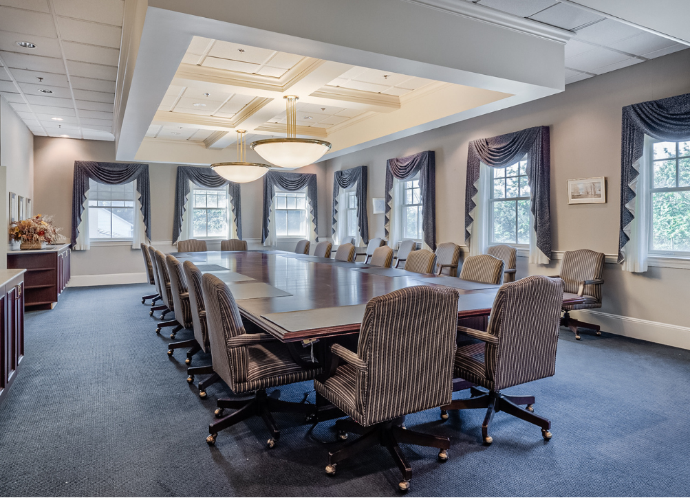 Large conference room with a long table, upholstered chairs, and windows with curtains