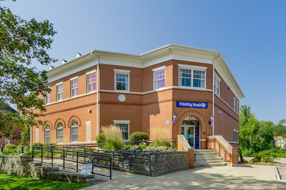 Brick building with blue sign and staircase, viewed from the street on a sunny day