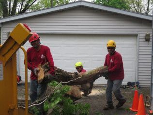 A group of men are carrying a large log in front of a garage.