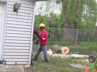 A man in a red shirt and yellow helmet is standing in front of a house.