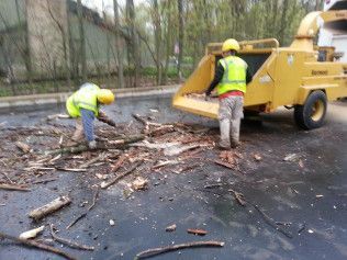 Two men are working on a tree chipper in a parking lot.