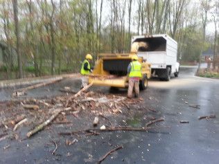 Two men are working on a tree chipper in a parking lot.