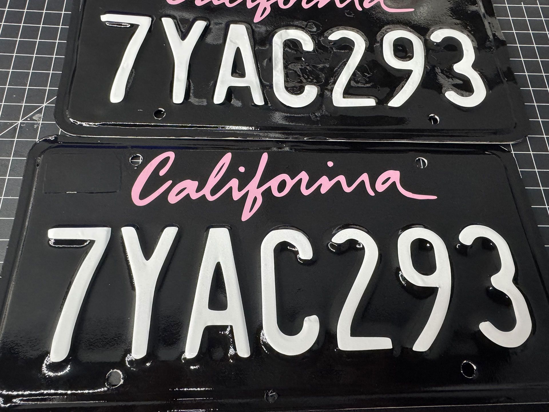 Two black California license plates with white numbers and letters: "7YAC293". Pink "California" script.