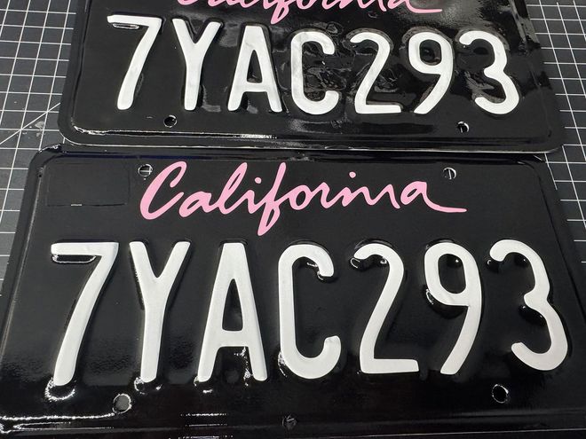 Two black California license plates with white numbers and letters: "7YAC293". Pink "California" script.