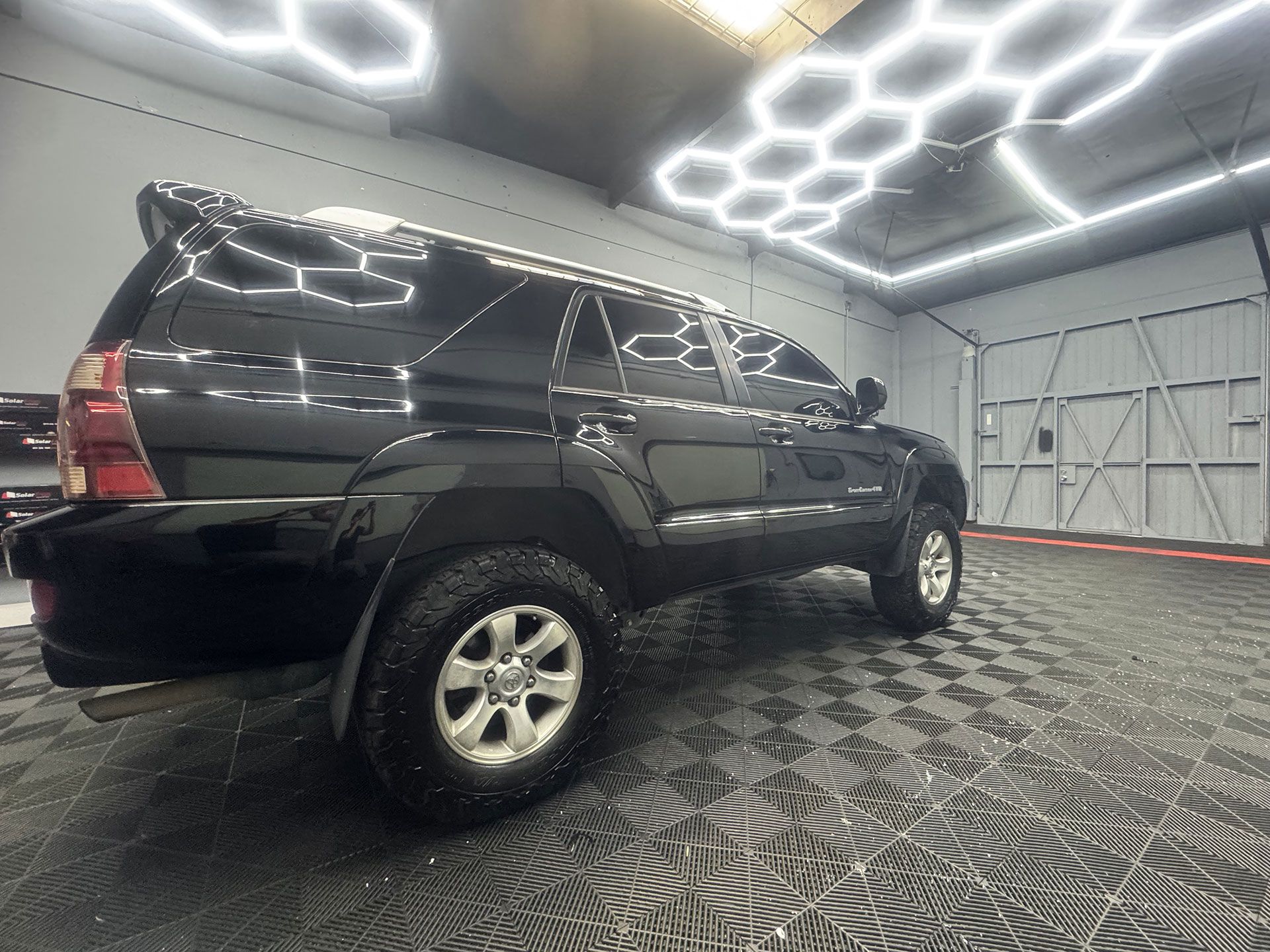 Black Toyota 4Runner SUV inside a garage with patterned flooring and honeycomb ceiling lights.