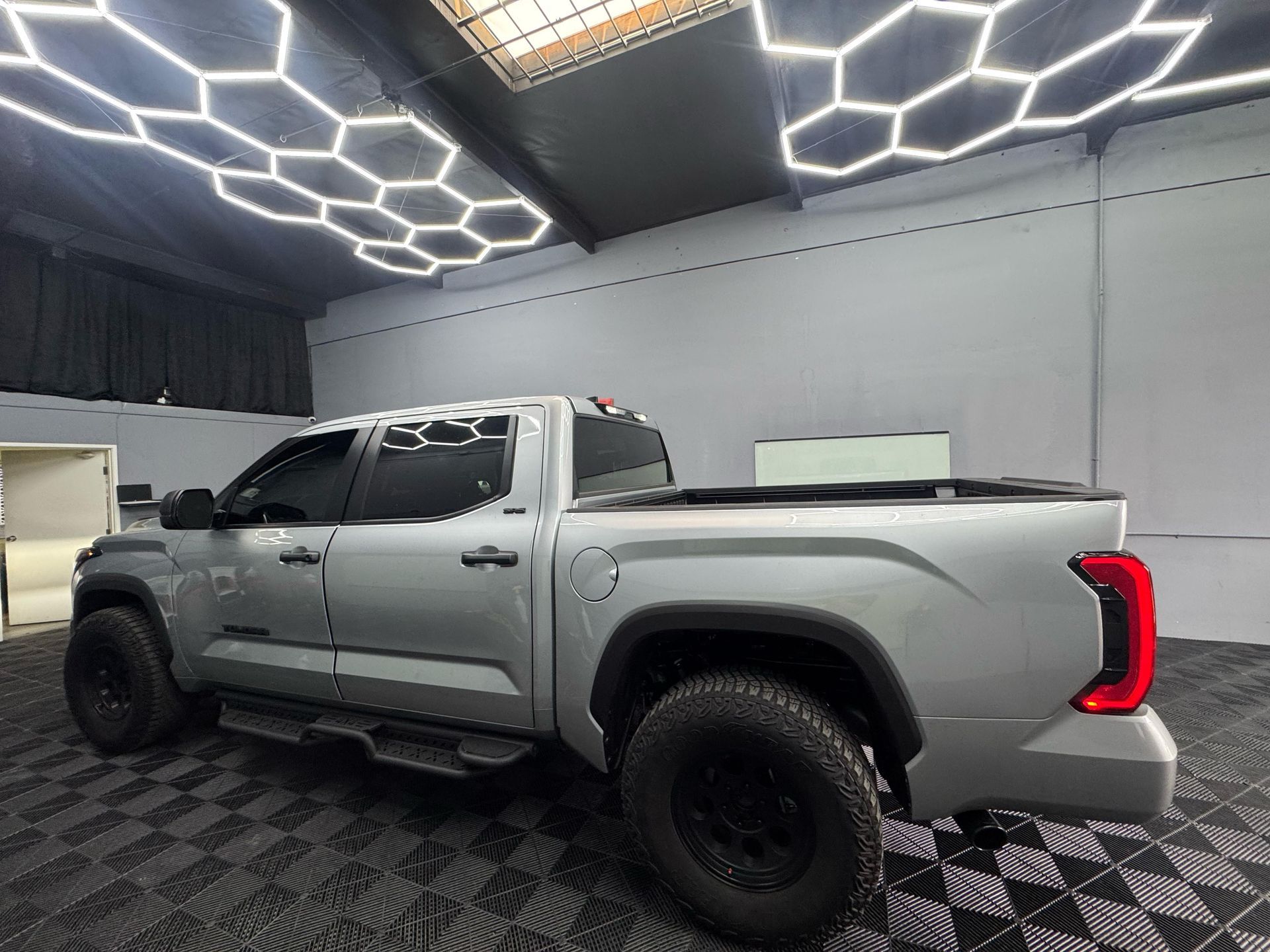 Silver Toyota Tundra pickup truck inside a garage with hexagon-shaped lights on the ceiling.