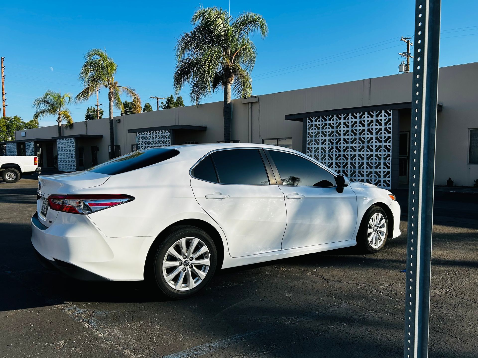 White sedan parked in front of a building with palm trees under a blue sky.