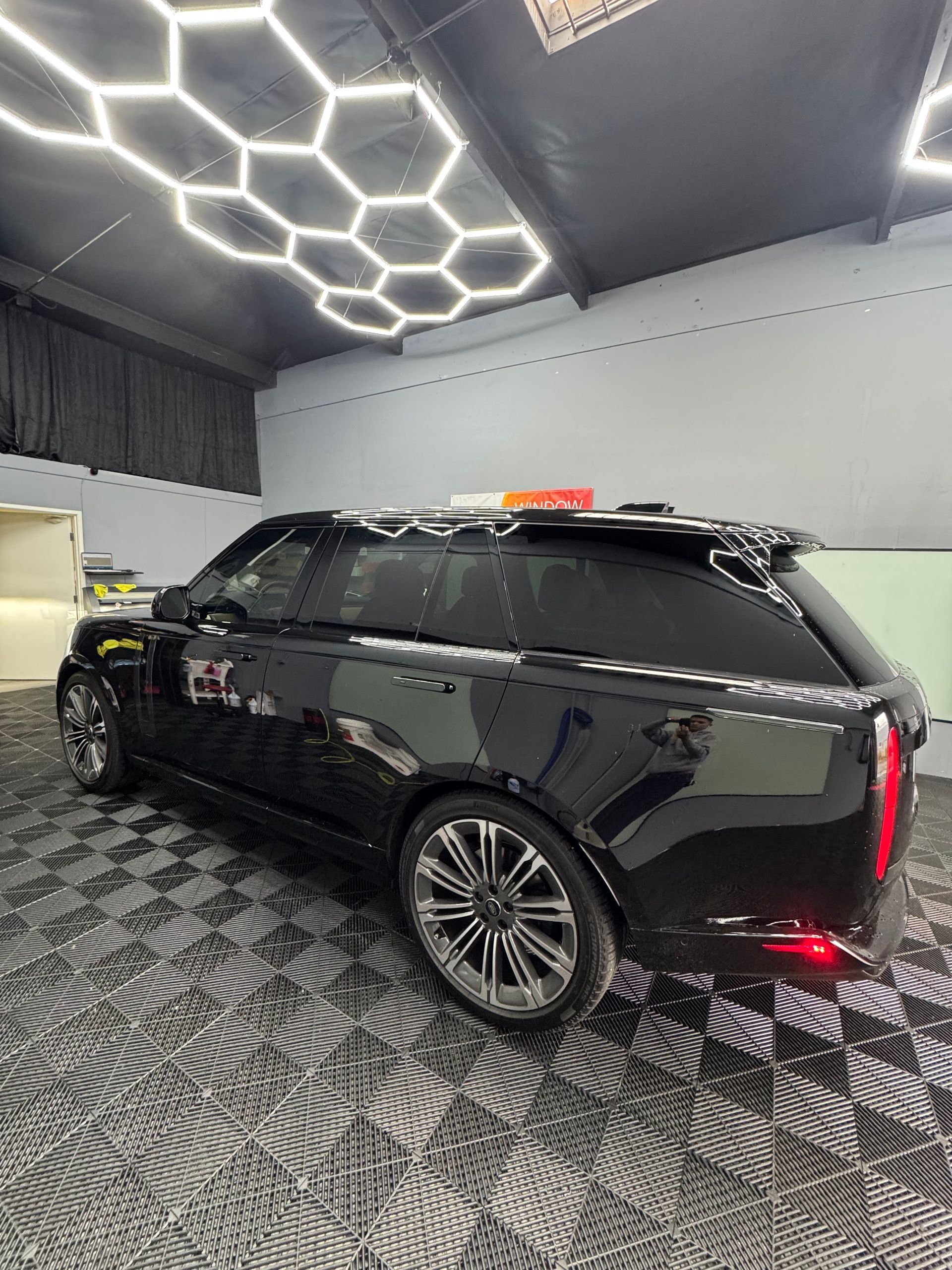 Black Range Rover SUV in a professional garage setting with honeycomb lighting and patterned floor.