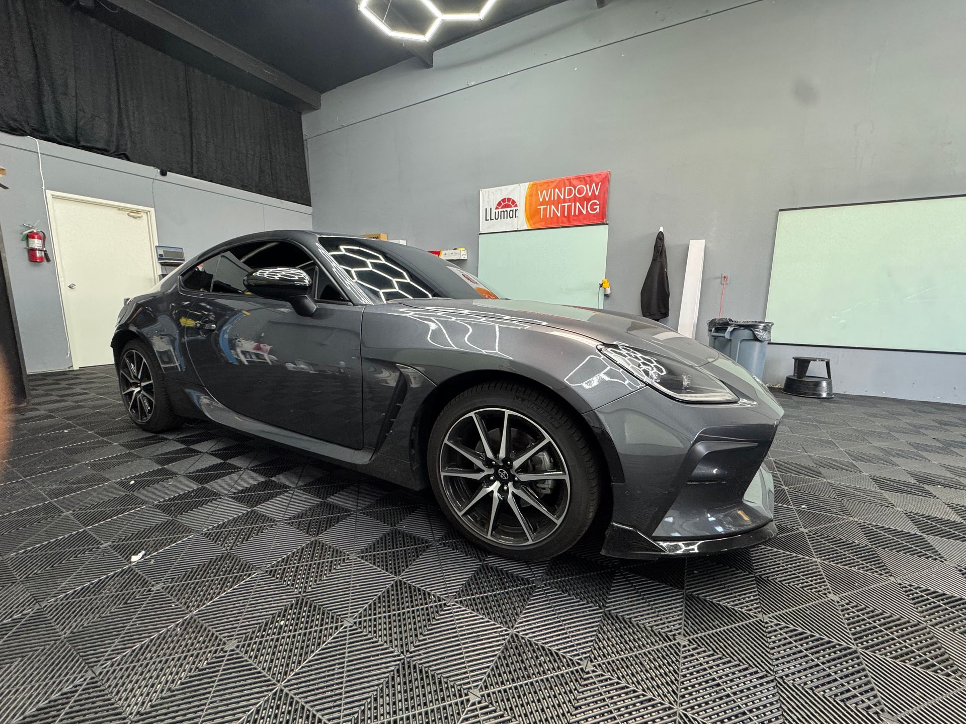 A grey sports car parked in a garage with tiled floor.