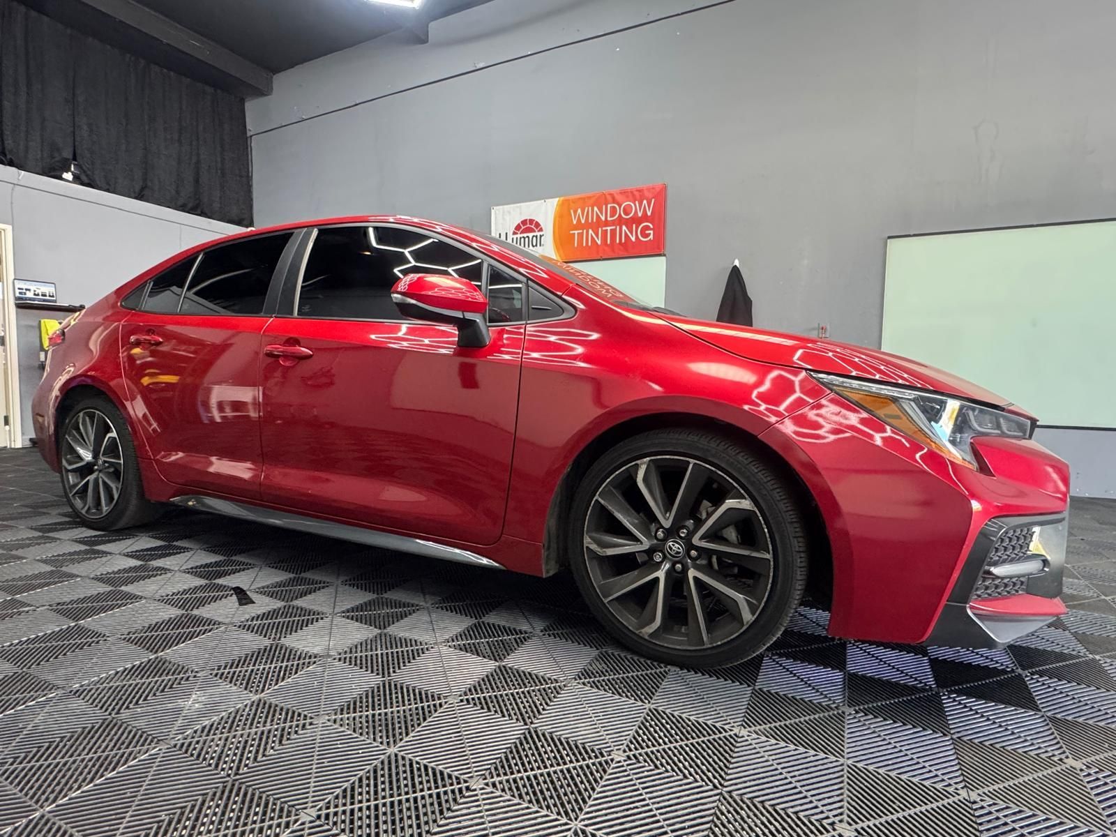 Red Toyota Corolla hatchback with tinted windows in a shop, parked on a checkered floor.