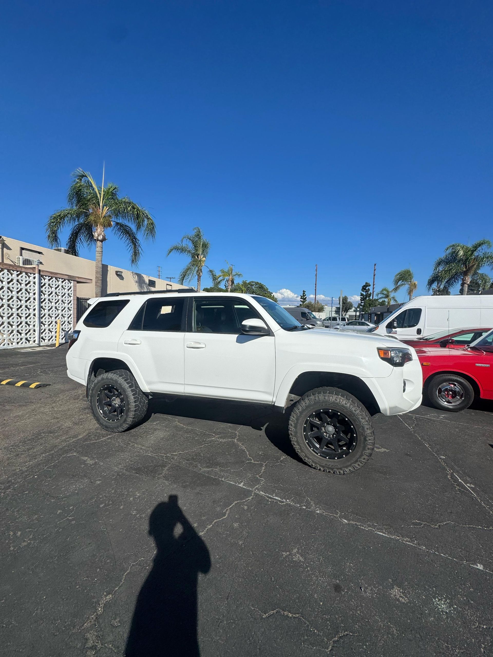 White lifted SUV on black wheels parked on asphalt, bright blue sky.
