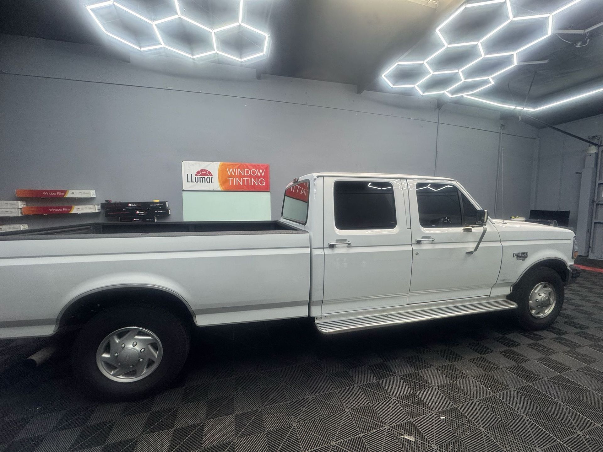 White Ford F-350 pickup truck in a well-lit garage, with chrome running boards and dark windows.