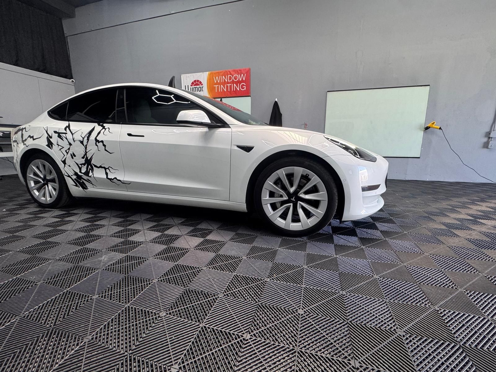 White Tesla Model 3 with black floral decals on checkered floor.