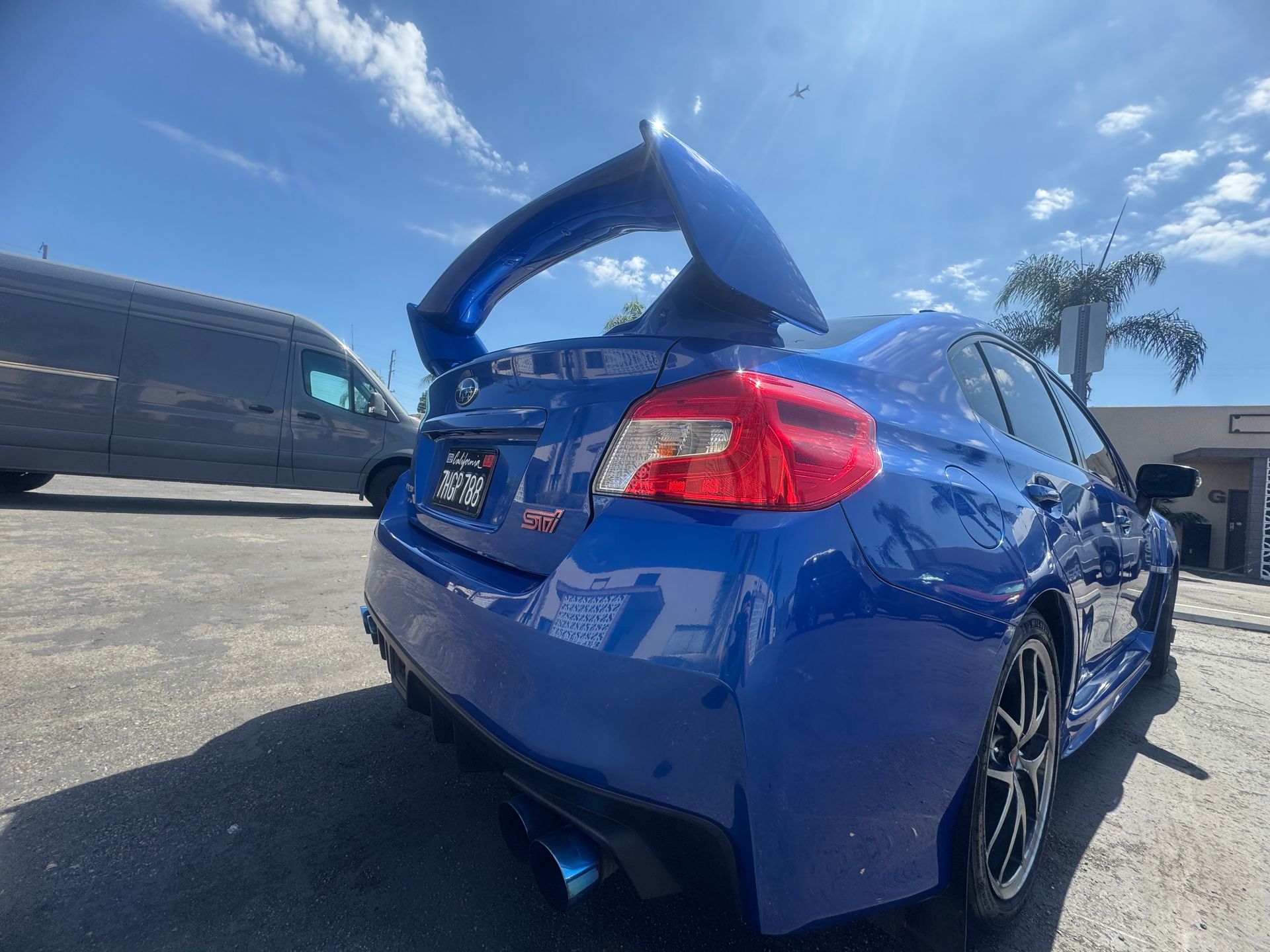Blue Subaru WRX STI with large rear wing parked outside under a blue sky.