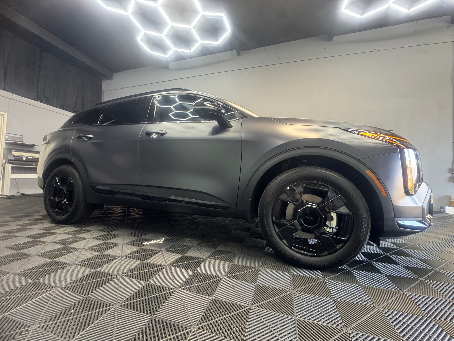 Gray Kia SUV with black wheels in a brightly lit showroom.