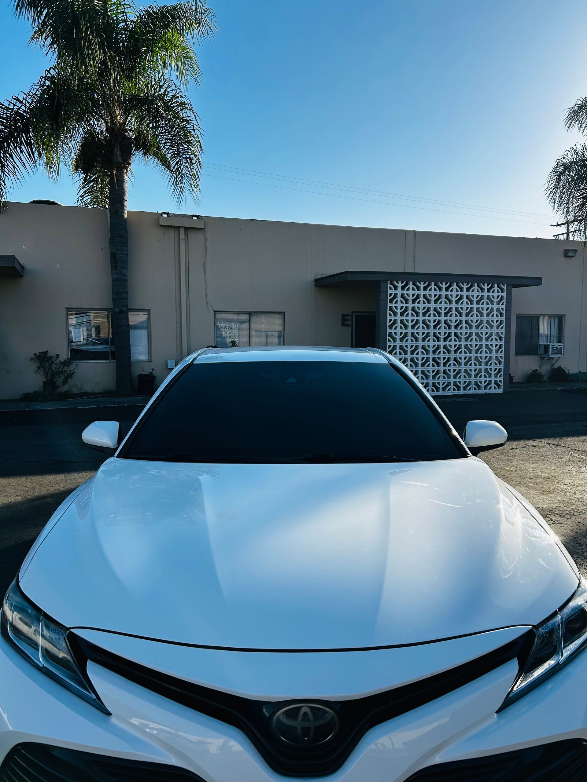 White Toyota car parked in front of a light-colored building under a sunny sky.