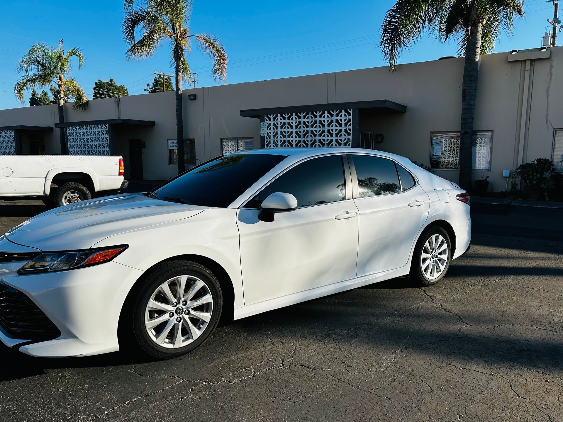 White Toyota Camry parked in front of a building with palm trees.