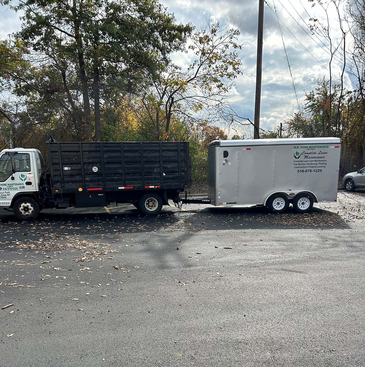 Black dump truck towing a white enclosed trailer on a gravel lot with trees in the background