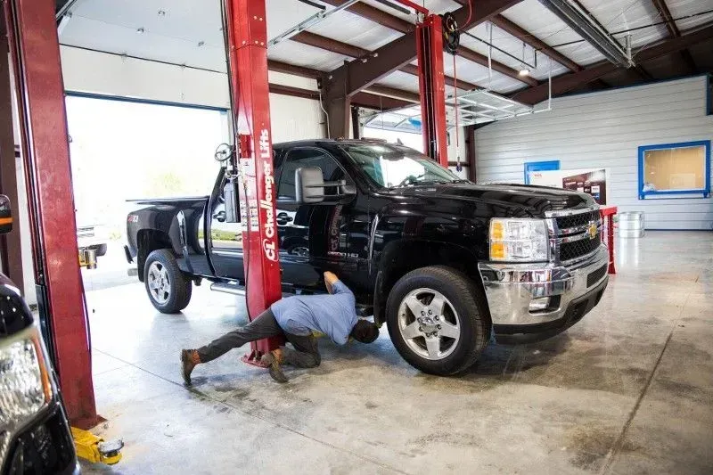 Mechanic working on a black pickup truck in a garage, using a lift.