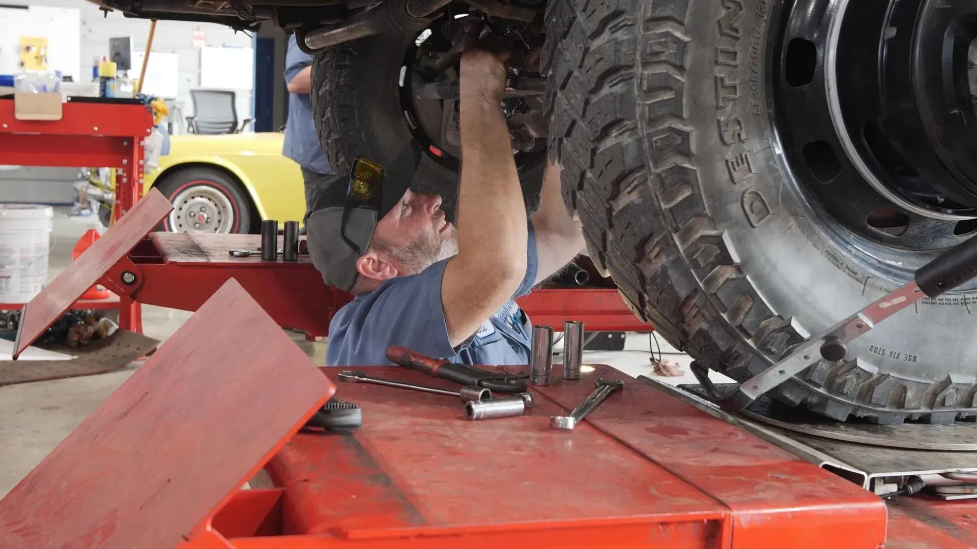 Mechanic working underneath a vehicle, using tools on a lift in a garage.