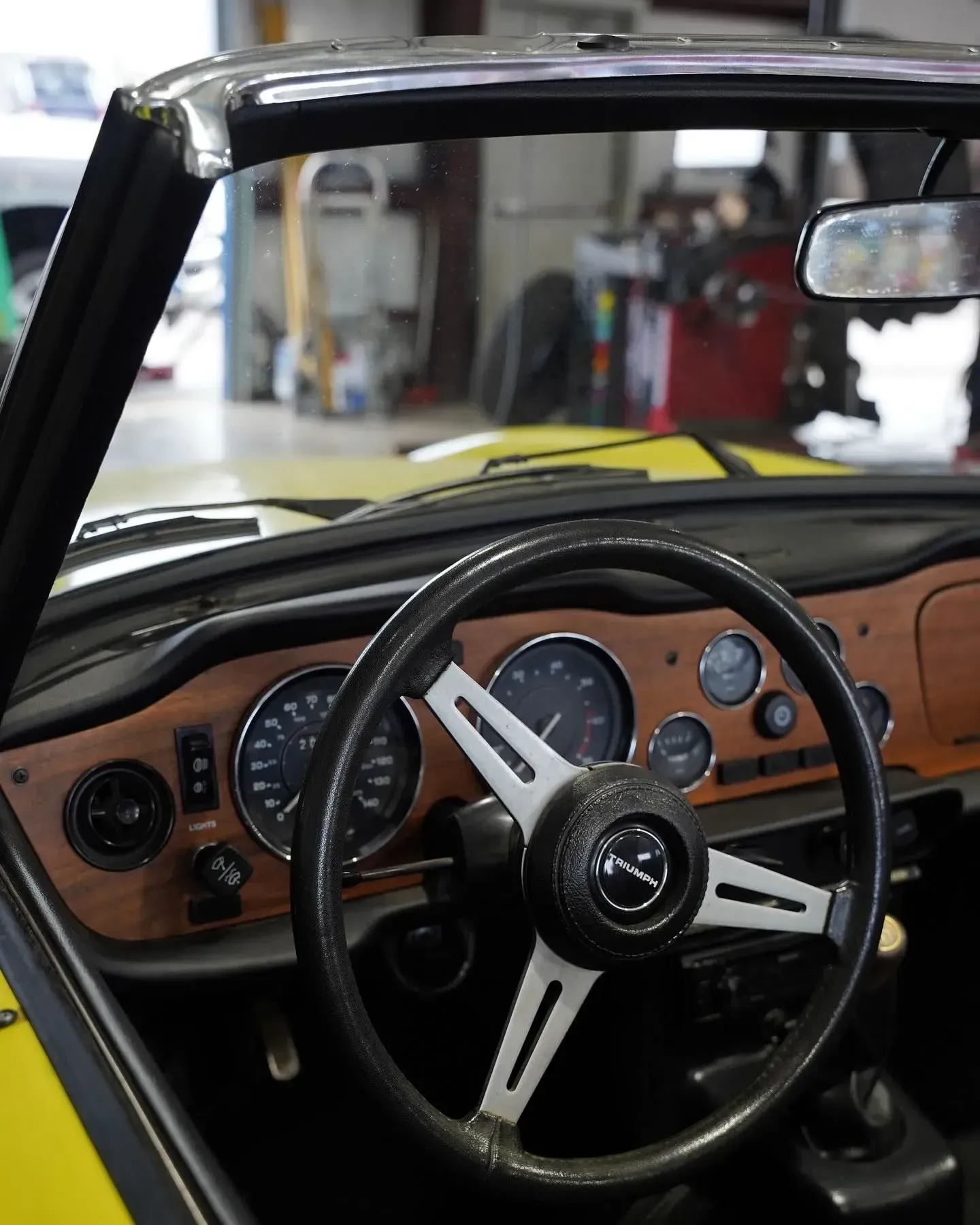 Interior view of a classic yellow sports car, featuring a wood dashboard and steering wheel, in a garage.