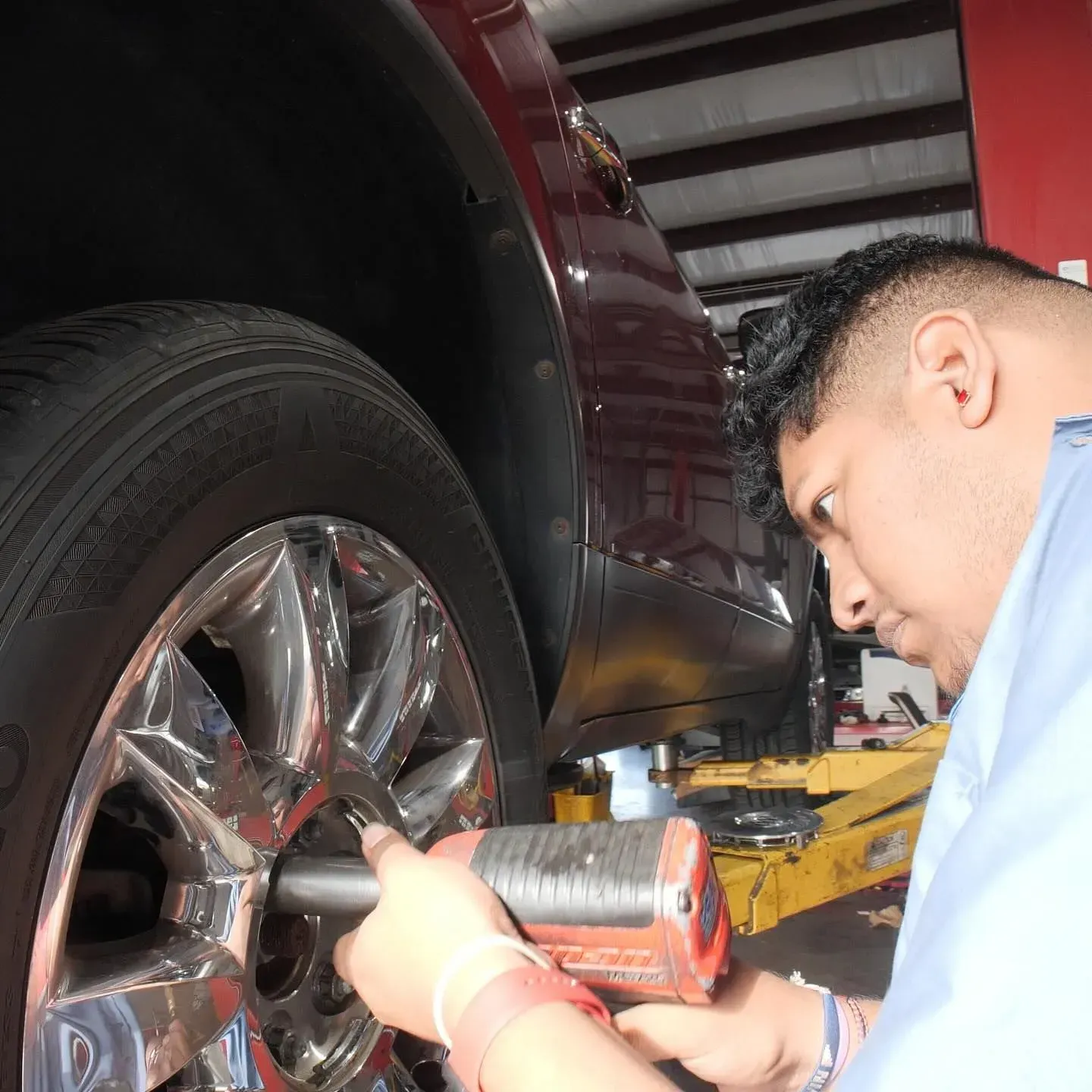 Mechanic using a power tool on a car wheel inside a shop.