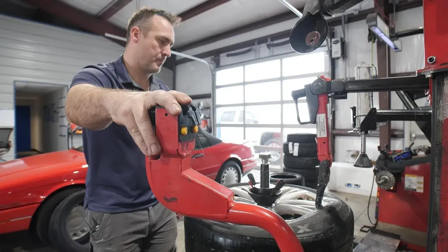 Mechanic using a red tool to work on a tire in a garage.