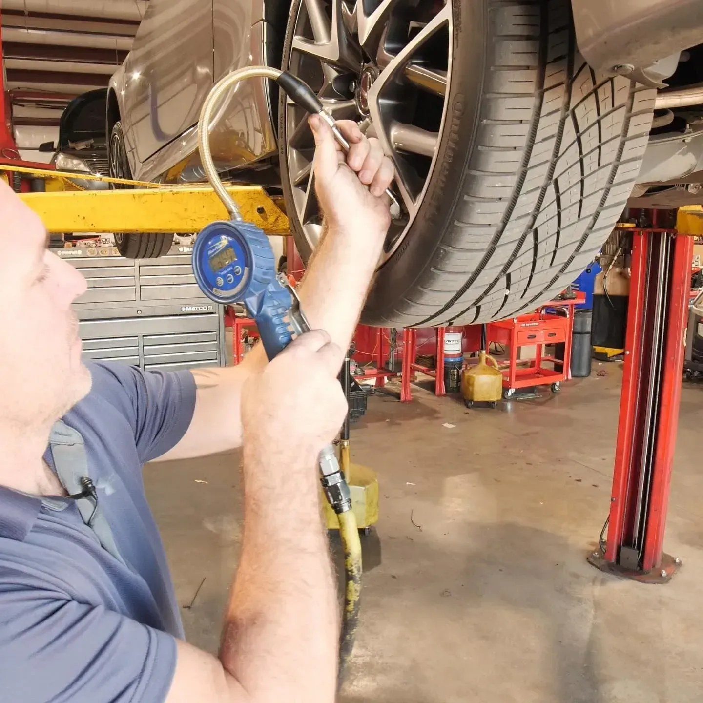 Man inflating a car tire in a garage, using a blue pressure gauge and yellow hose.