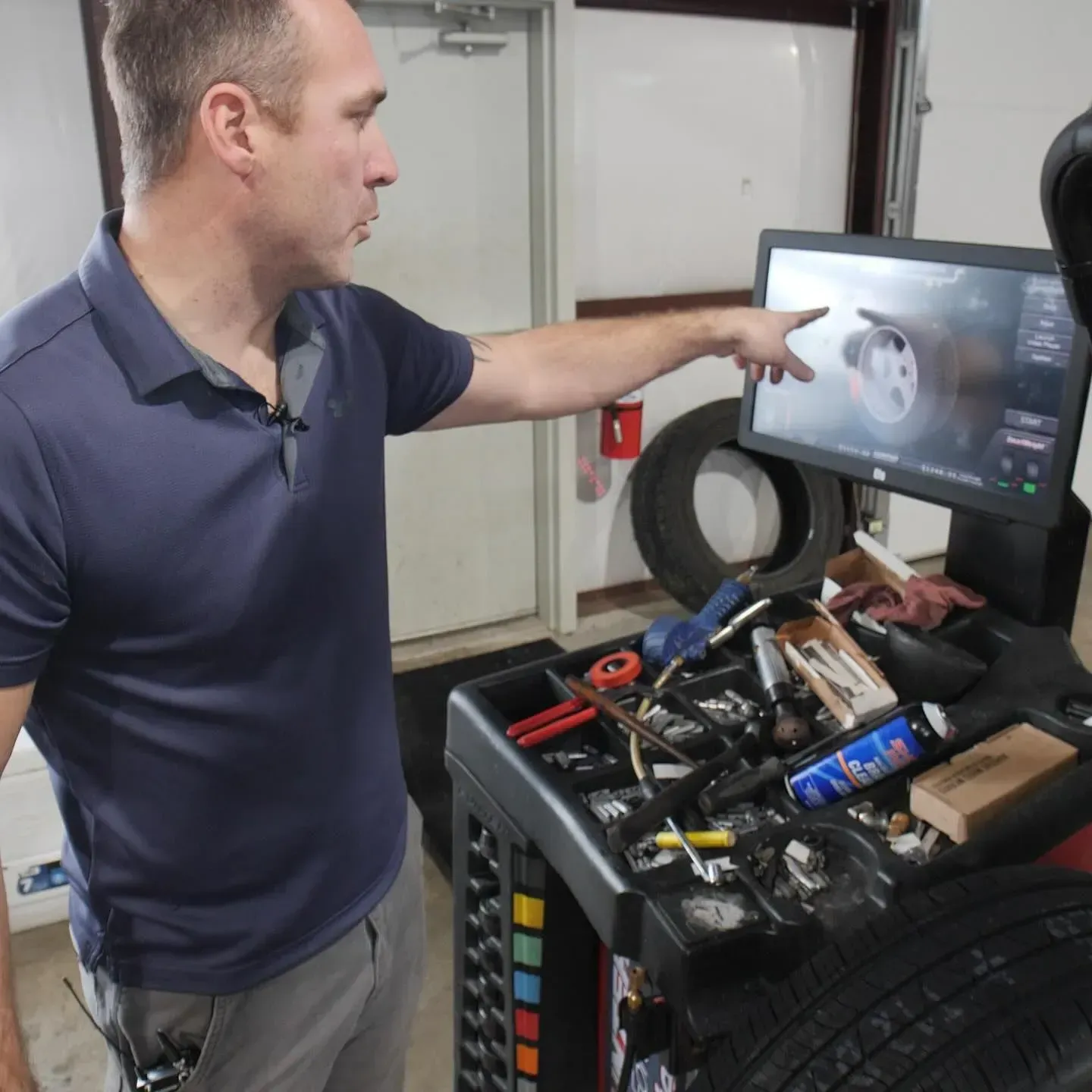 Mechanic pointing at tire display in a garage, explaining tire balance.
