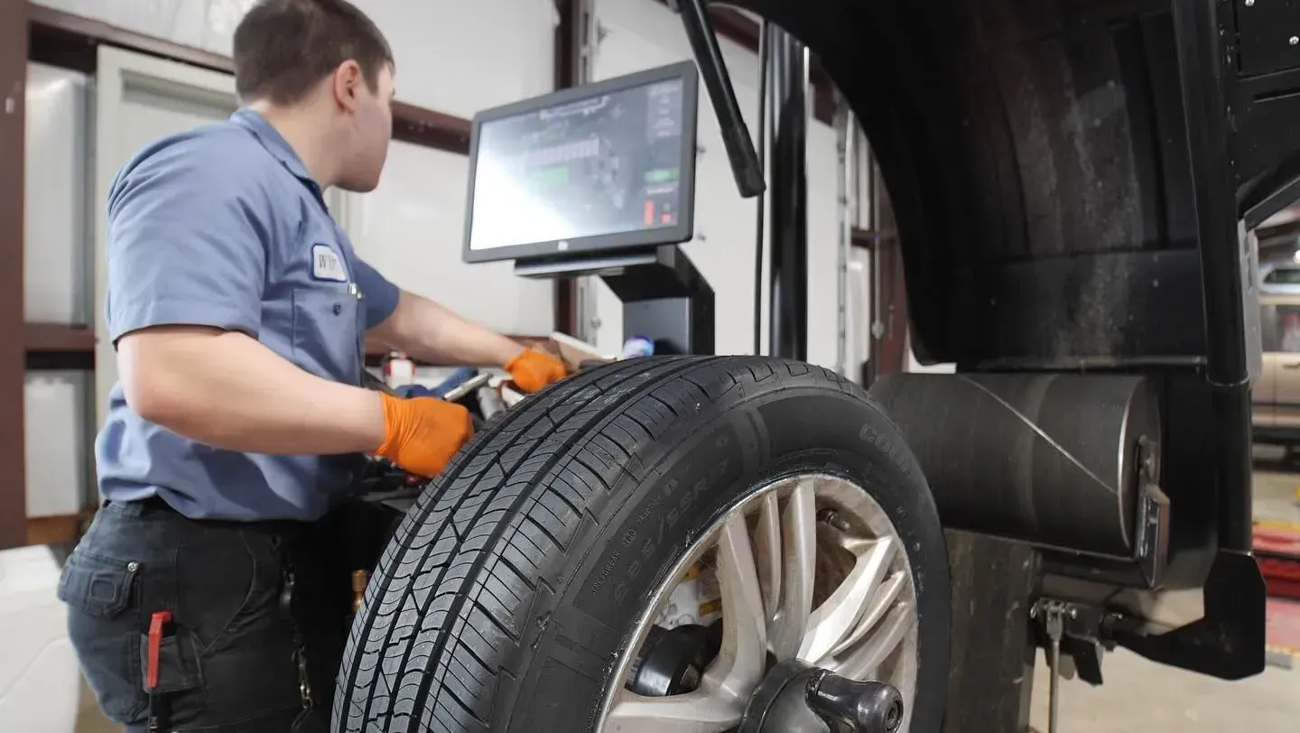 Mechanic balancing a car tire with a computer monitor in a garage.